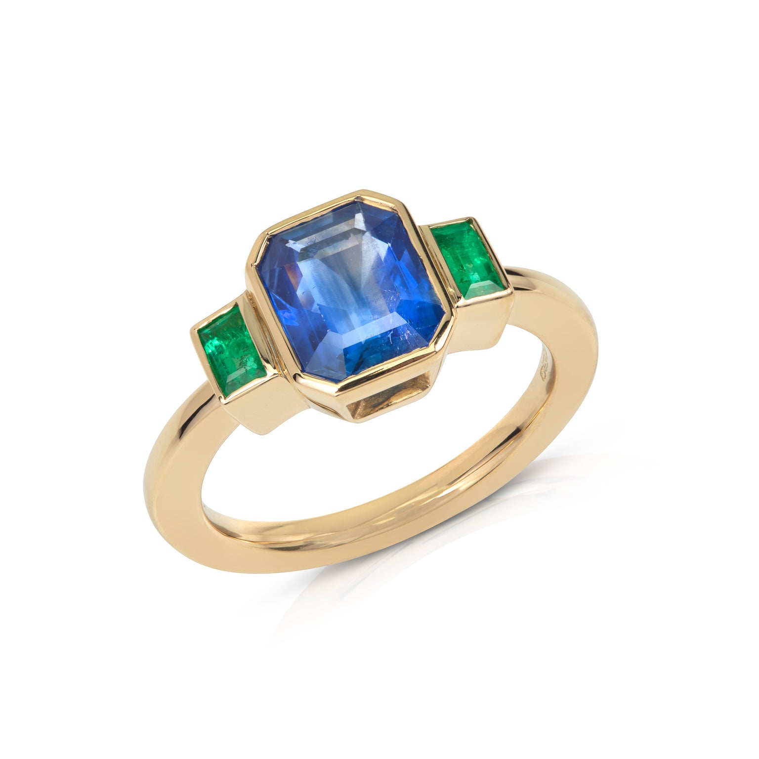 Gold ring with a central blue emerald-cut sapphire, flanked by two baguette-cut emeralds on a white background