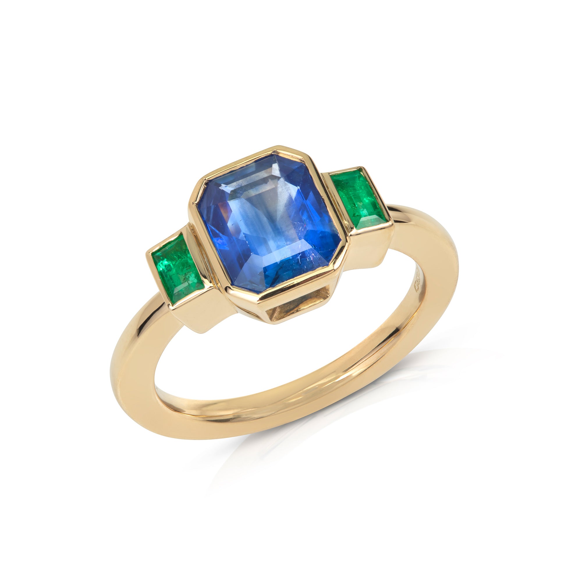 Gold ring with a central blue emerald-cut sapphire, flanked by two baguette-cut emeralds on a white background