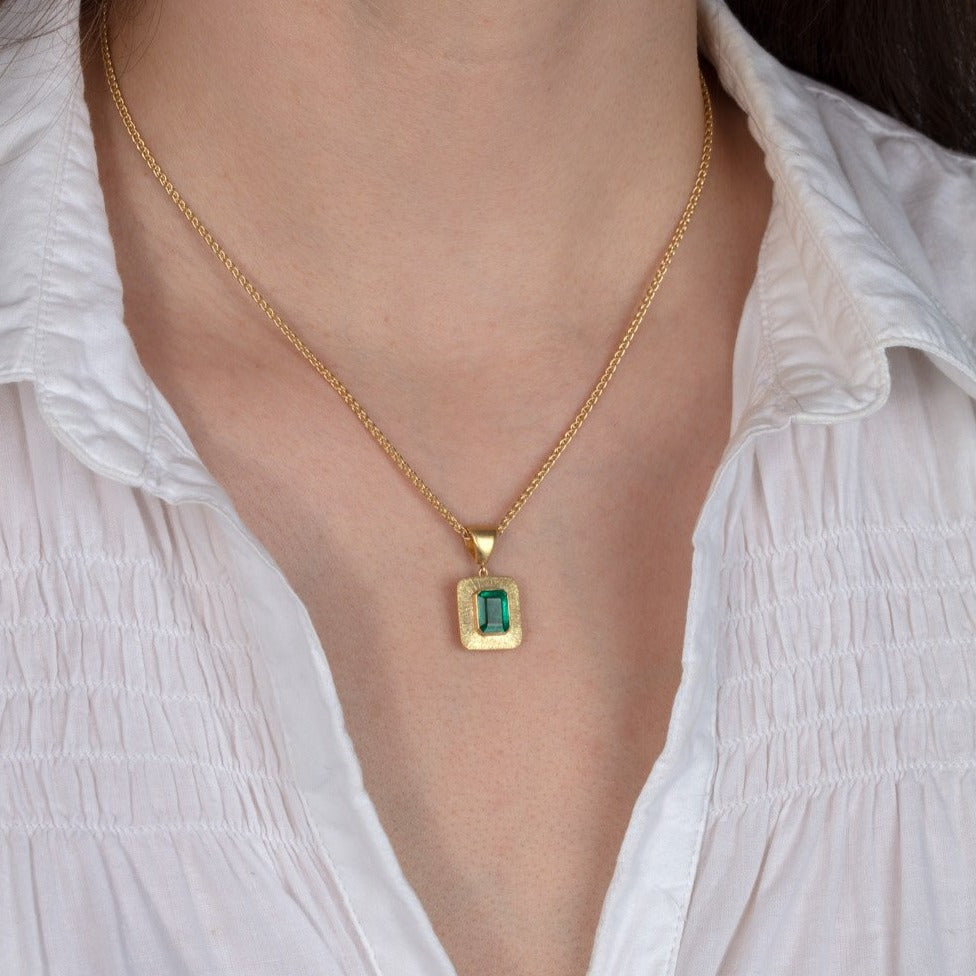 gold and emerald pendant necklace shown on a model