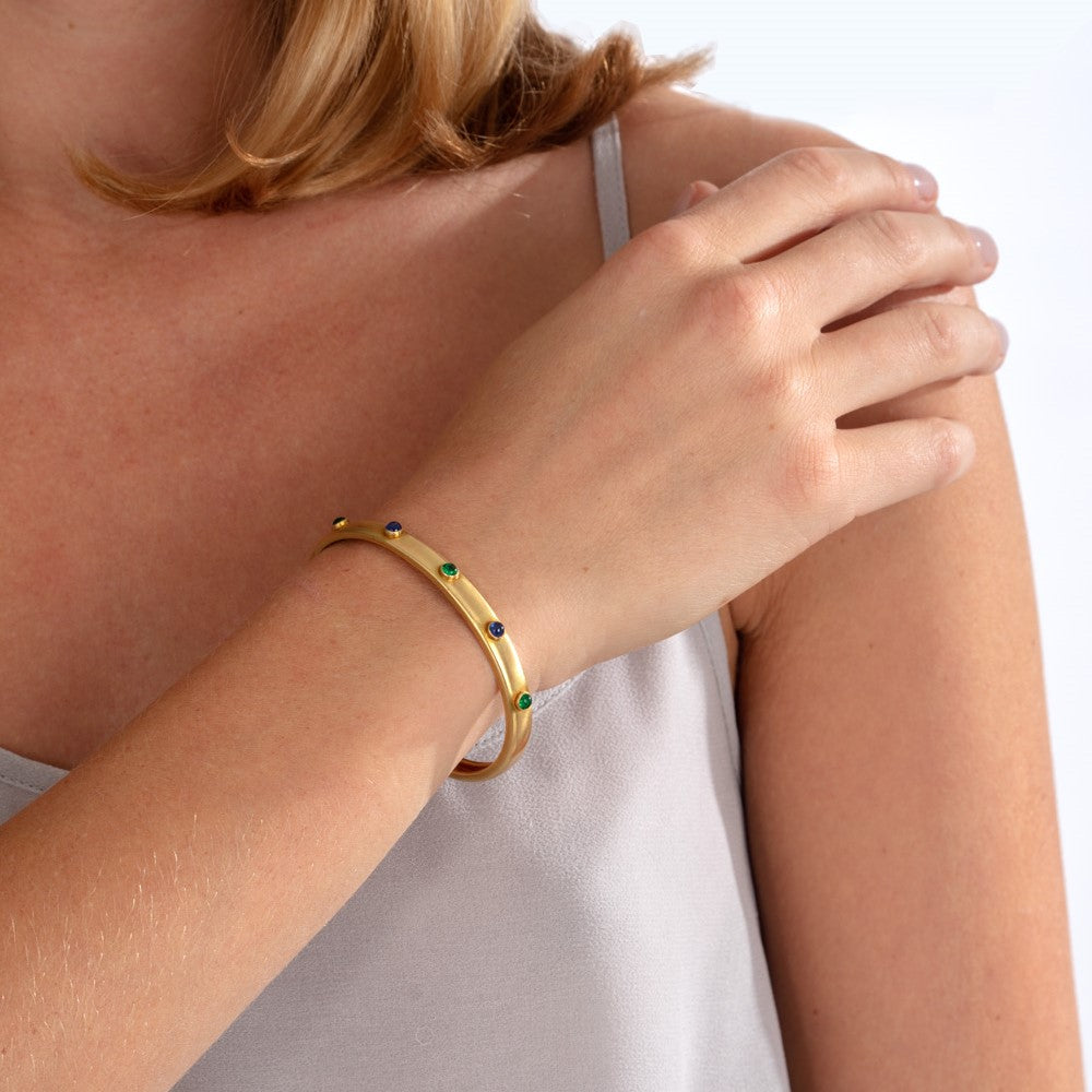 Model pictured wearing gold bangle set with emerald and sapphire cabochons