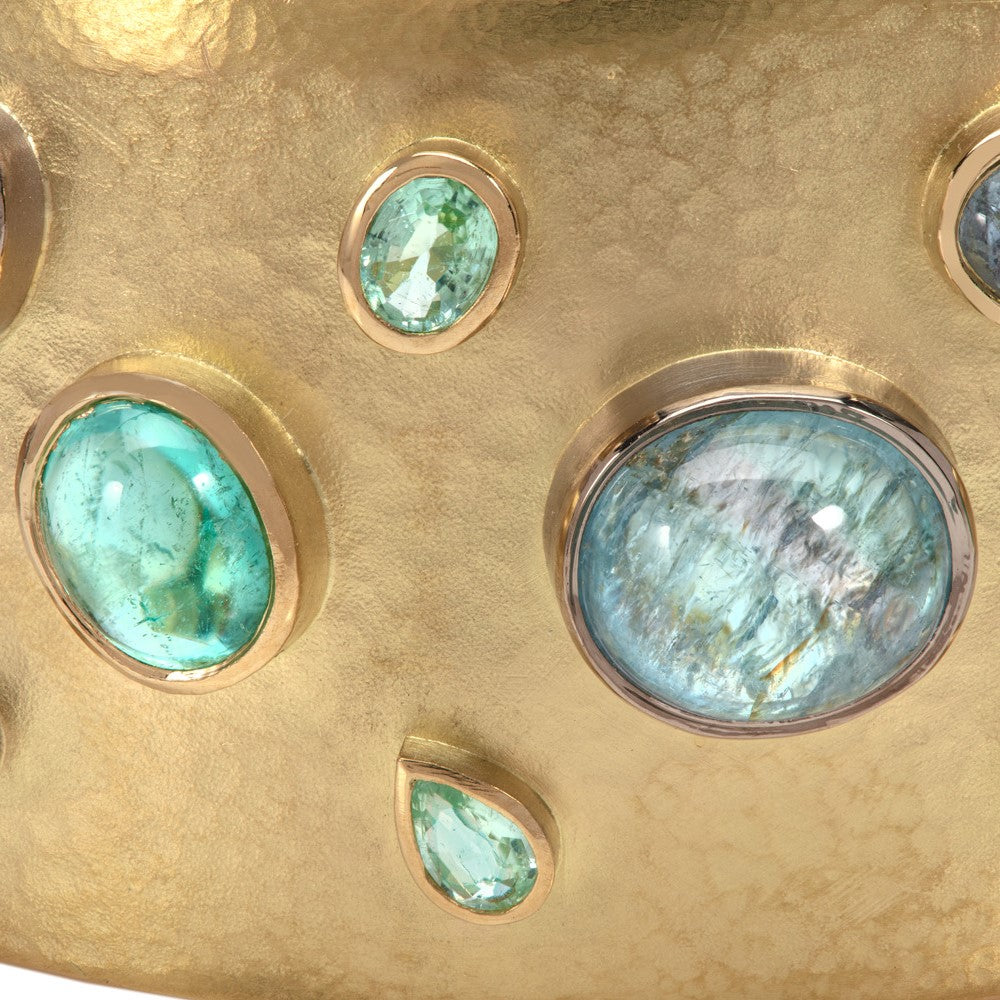 Close up of yellow gold cuff bangle set with paraiba tourmalines and diamonds showing the detail