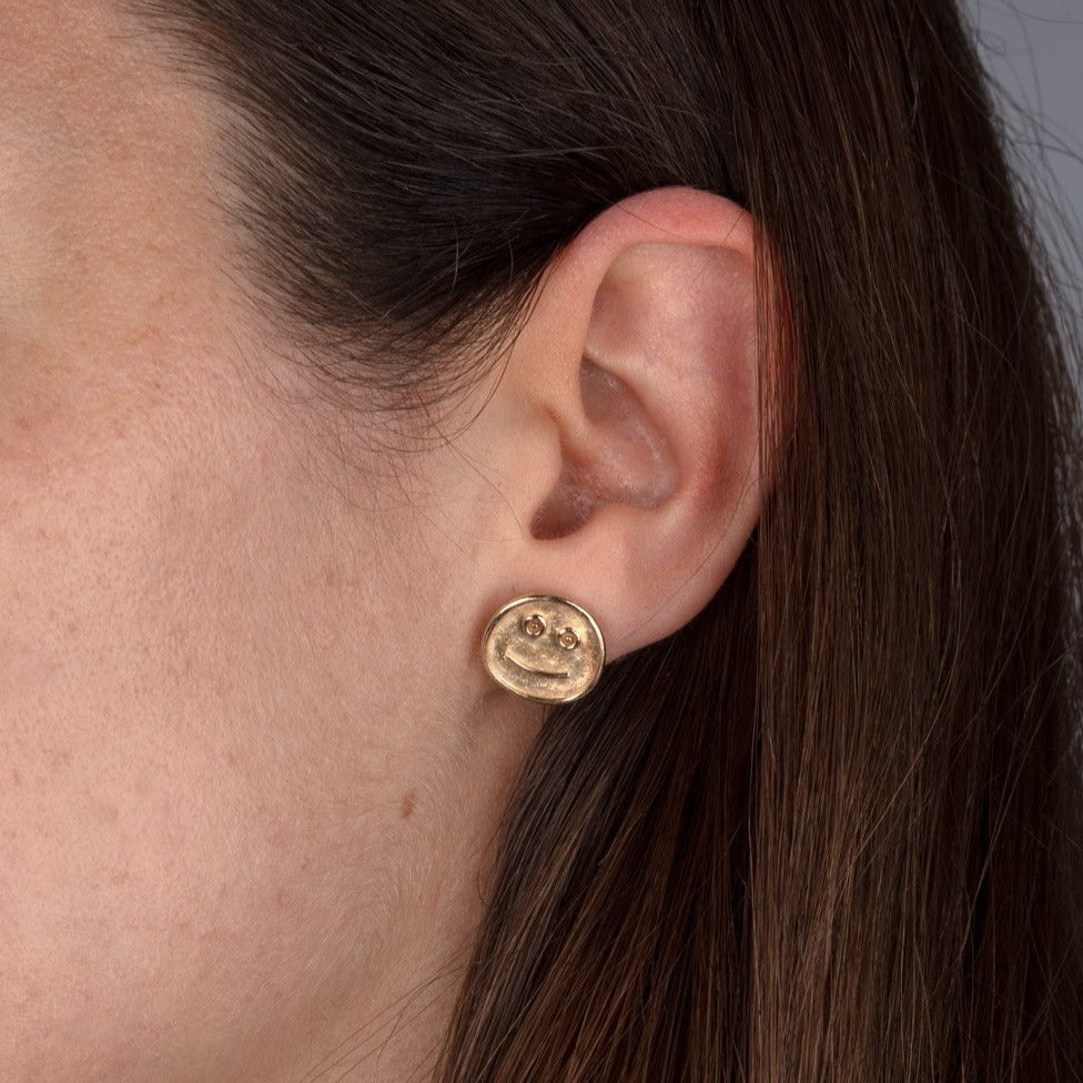 gold smiley face stud earrings shown on model