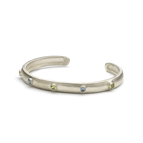 Silver wrap around bangle set with blue topaz and peridot, matte finish, pictured on a white background